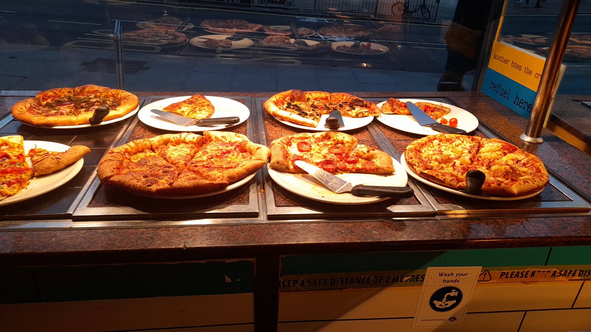 Casa Della Pizza's window counter with pizzas and serving utensils on white plates